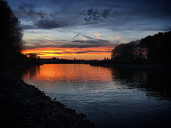 Dramatic Sunset Over River with City Skyline Silhouette