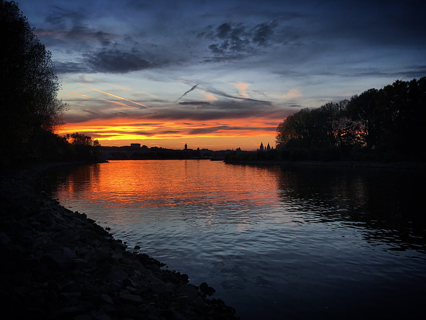 Dramatic Sunset Over River with City Skyline Silhouette