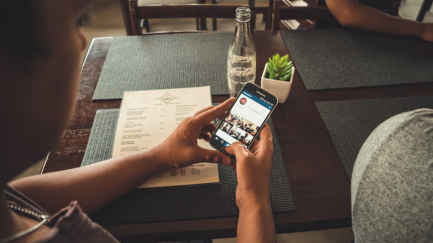 Man Using Smartphone At Cafe Table With Menu And Drink