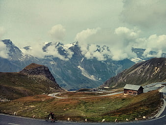 Cyclist on winding mountain road with snowy peaks