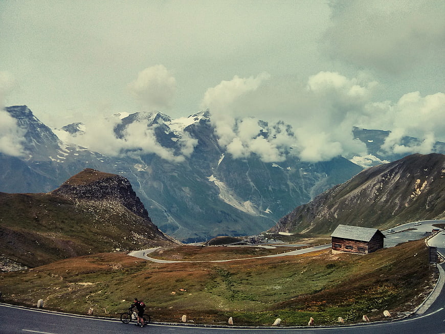 Cyclist on winding mountain road with snowy peaks