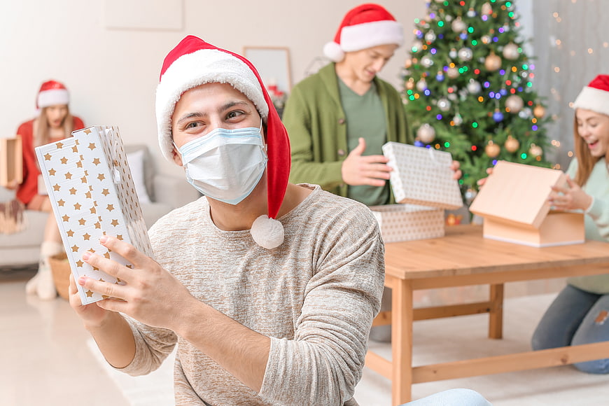 Man with Santa Hat and Face Mask Opening Christmas Gift