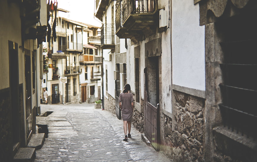 Woman Walking Down Narrow Cobblestone Street in Old Town