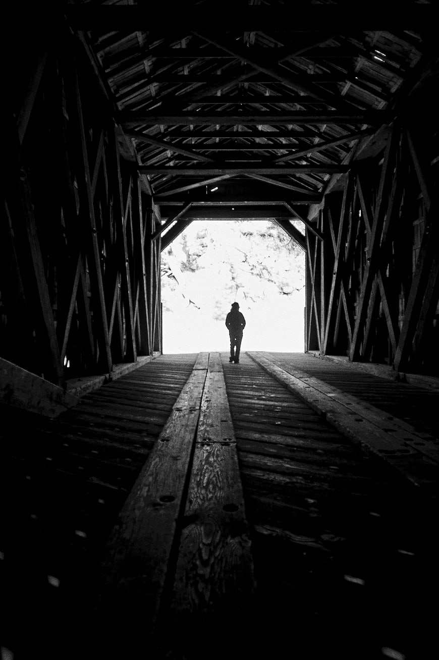 Silhouette of Person Walking Through Dark Covered Wooden Bridge