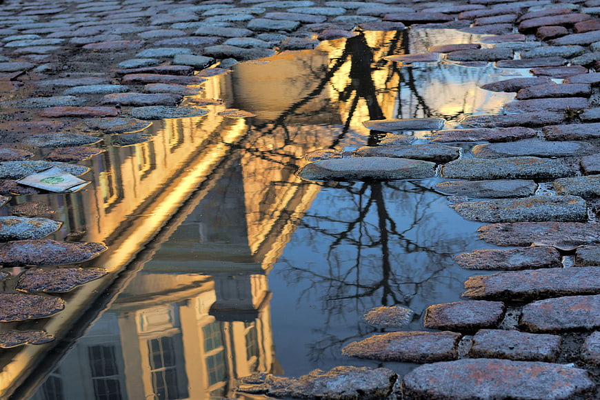 Golden hour reflection of a building in a puddle on a cobblestone street