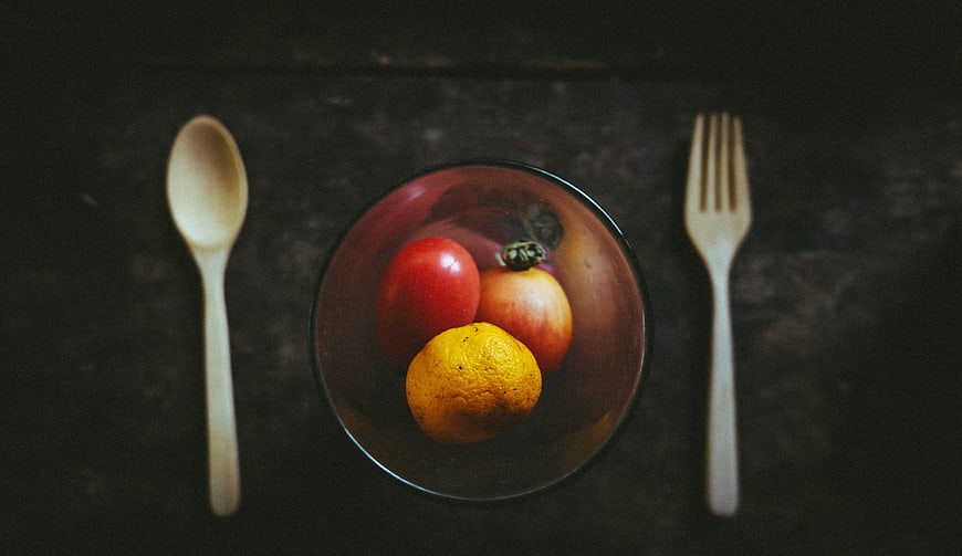 Top view of fresh fruit in a glass bowl with wooden cutlery