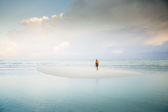 Lone man walking on sandbar in turquoise ocean