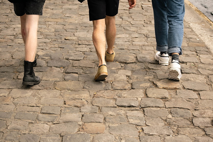 Three people walking on cobblestone street from behind