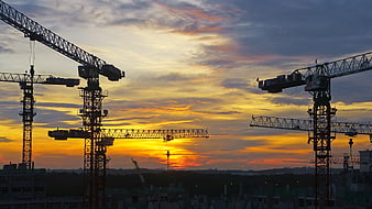 Silhouetted Construction Cranes Against Vibrant Sunset Sky