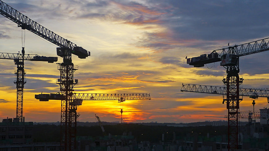 Silhouetted Construction Cranes Against Vibrant Sunset Sky