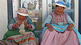 Two elderly Peruvian women in traditional dress knitting and smiling