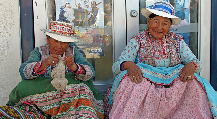Two elderly Peruvian women in traditional dress knitting and smiling
