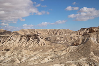 Vast arid desert landscape with eroded hills and blue sky
