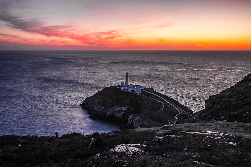 Lighthouse on Rocky Cliff at Vibrant Sunset Over Ocean