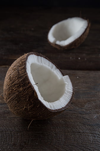 Cracked coconut halves on rustic dark wood background