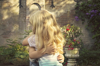 Embracing children in a sunlit garden with vintage brick wall background