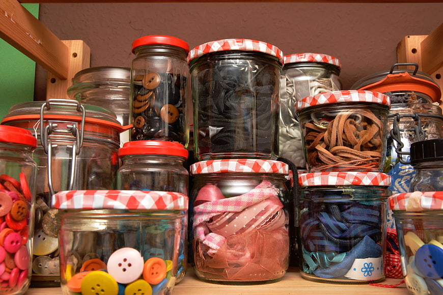Organized sewing supplies in glass jars on wooden shelf