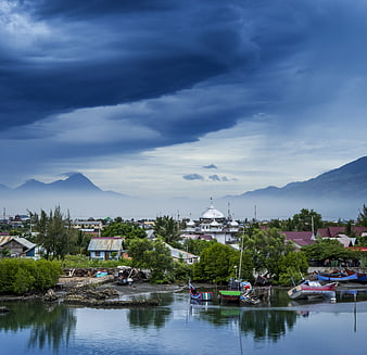 Dramatic storm clouds over coastal village with boats and mosque