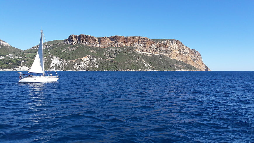 Sailboat sailing on blue sea near rocky cliffs