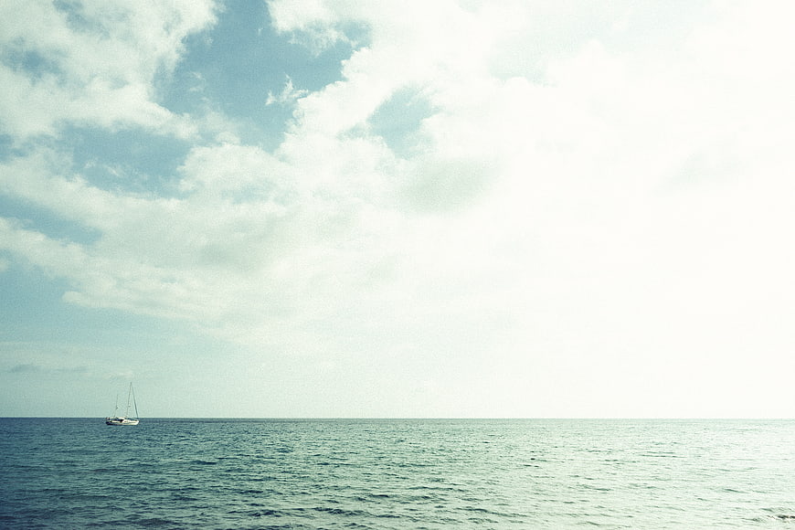 Lone Sailboat on Calm Ocean Under Bright Cloudy Sky