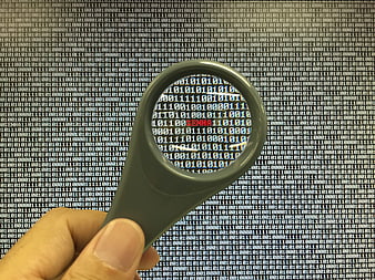 Magnifying glass inspecting binary code on computer screen