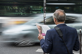Senior man reading newspaper at busy bus stop