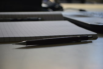 Black mechanical pencil on notebook with laptop background