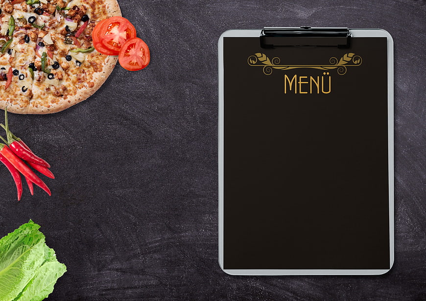 Pizza and fresh vegetables with blank menu clipboard on dark background
