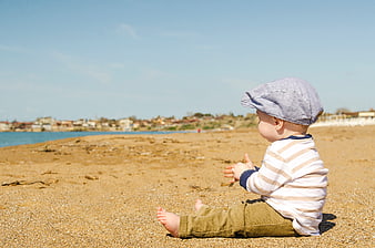 Baby Boy Sitting on Sandy Beach Looking at Ocean