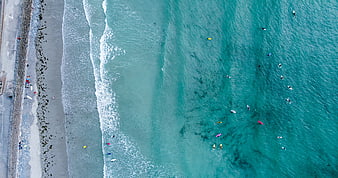 Aerial view of surfers in turquoise ocean waves near beach