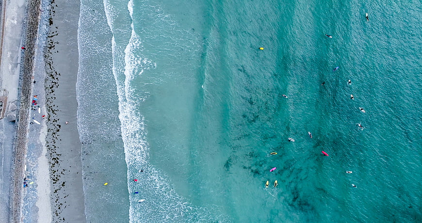 Aerial view of surfers in turquoise ocean waves near beach