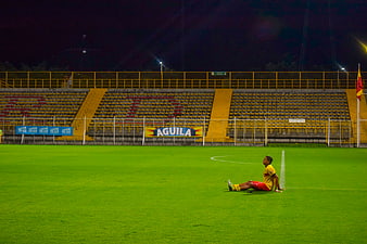 Lonely soccer player sitting on grass in empty stadium at night
