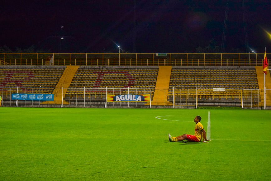 Lonely soccer player sitting on grass in empty stadium at night
