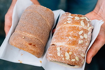 Hands holding two fresh pastries in white paper trays
