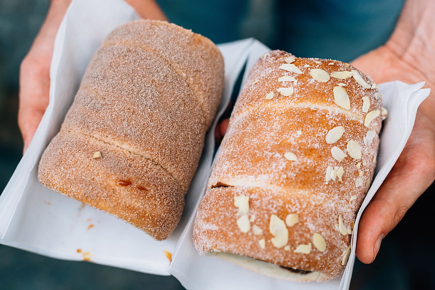 Hands holding two fresh pastries in white paper trays