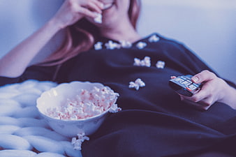 Woman eating popcorn and holding remote control on bed