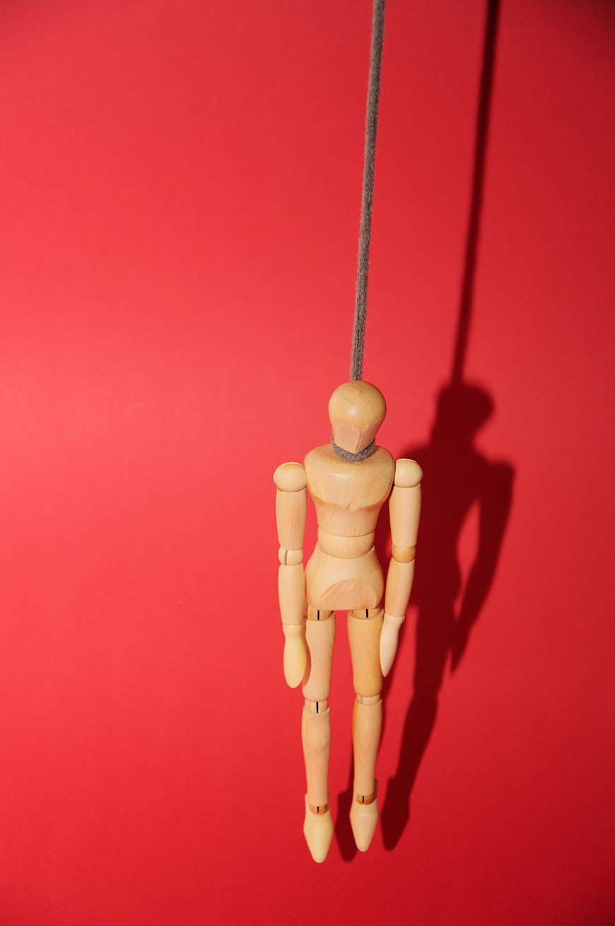 Wooden Mannequin Hanging by Rope on Red Background