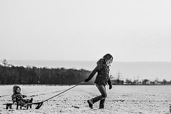 Mother pulling child on sled in snowy winter field