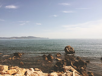 Sunny coastal landscape with rocky shore and blue sea horizon