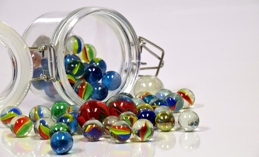 Colorful glass marbles spilling from a jar on white background