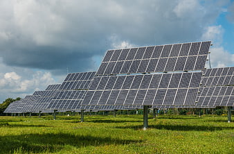 Solar panels in a green field under cloudy sky