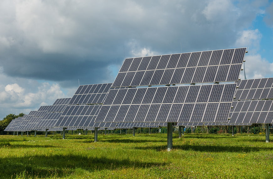 Solar panels in a green field under cloudy sky