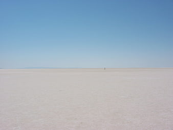 Lone figure walking across vast white salt flat landscape