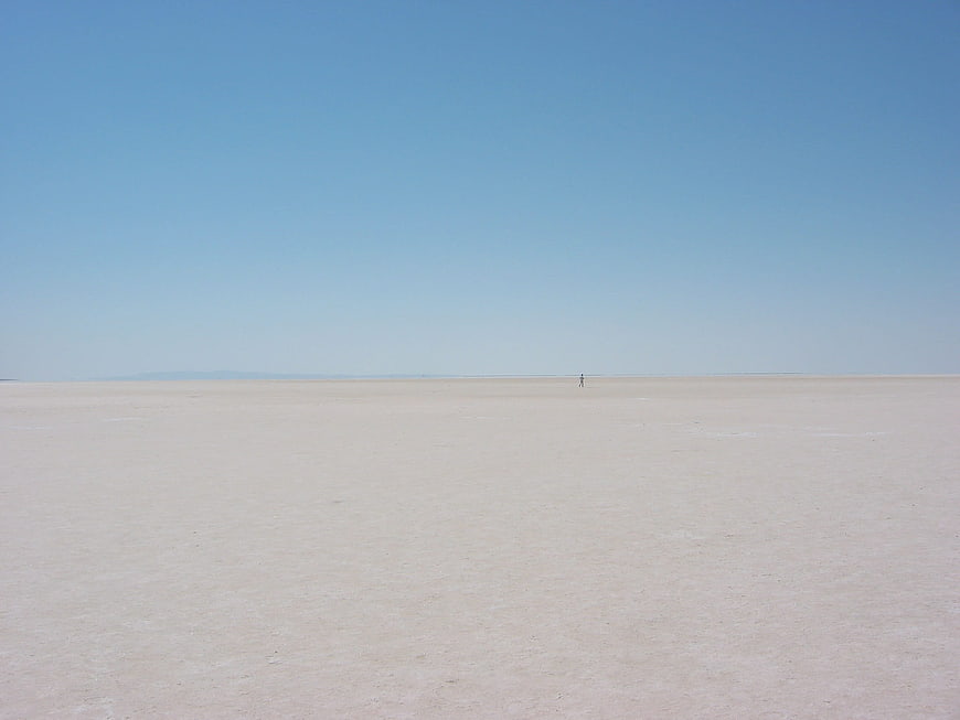 Lone figure walking across vast white salt flat landscape