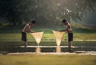 Two boys fishing with nets in a river at sunset
