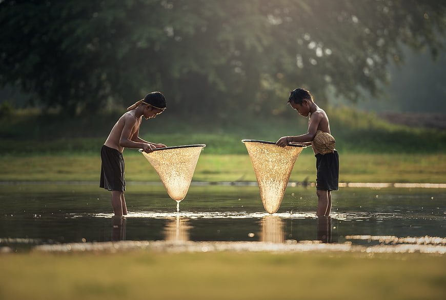 Two boys fishing with nets in a river at sunset