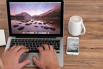 Top-Down View of Hands Typing on Laptop with Coffee and Smartphone on Wooden Desk