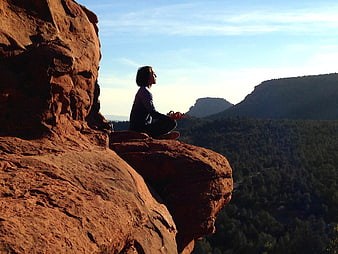 Woman meditating on red rock cliff overlooking forest valley