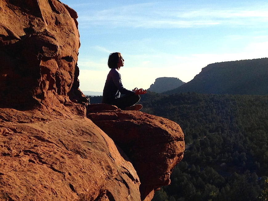 Woman meditating on red rock cliff overlooking forest valley