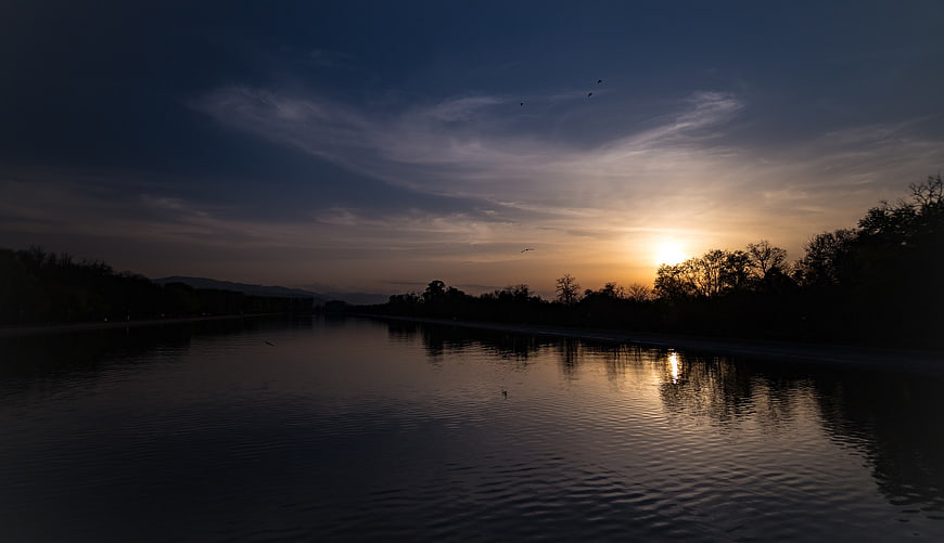 Serene Sunset Reflection on Calm River with Silhouetted Trees